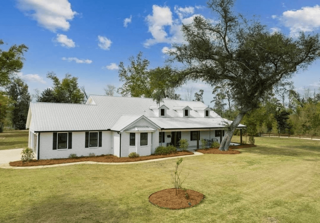 White farmhouse with a clean standing-seam metal roof and manicured lawn